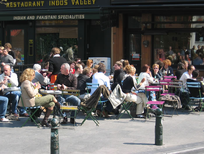 människor på café Bild: Människor som sitter på ett utomhusservering längs en trottoar.